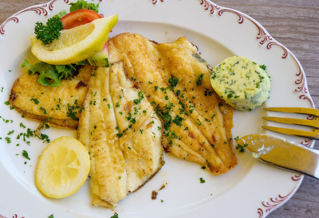 fried plaice fillet with herb butter and lemon on a plate, typical food in northern germany at the coast, high angle view, above
